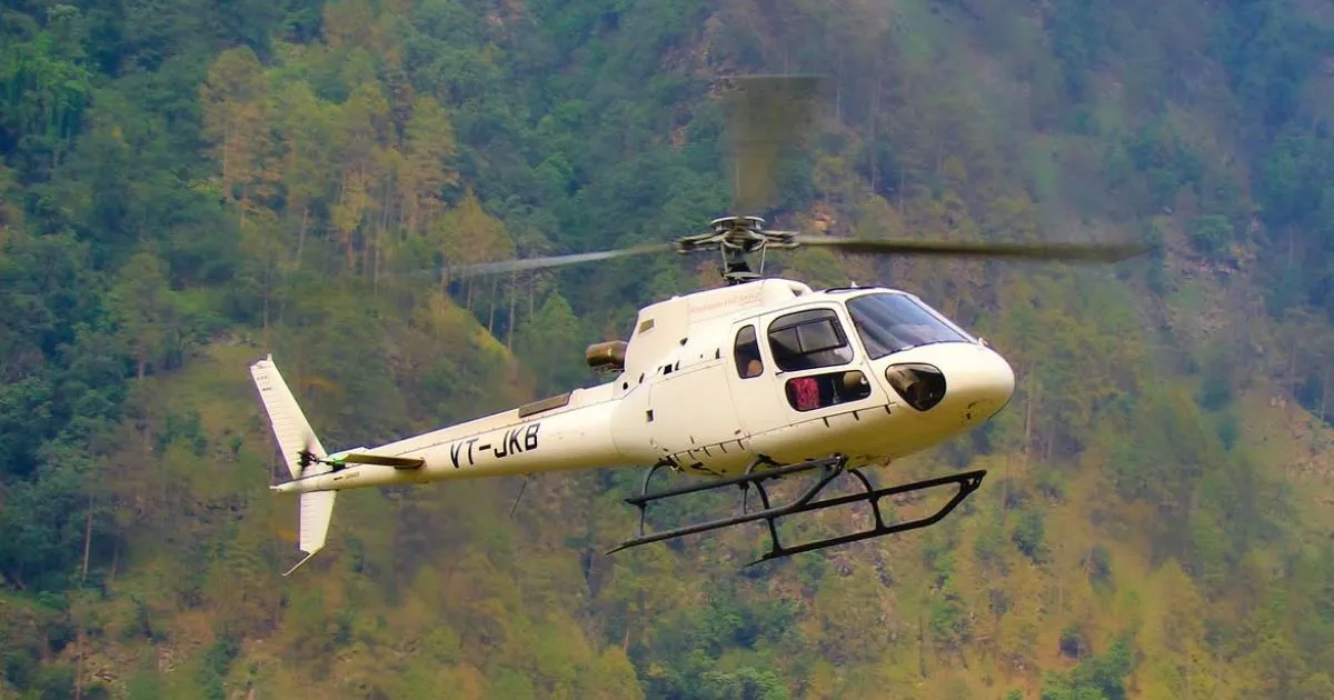Char Dham Yatra Registration, Route Map, Itinerary, Packages & Helicopter Booking 10 A white helicopter flies smoothly across a lush mountainous landscape covered in green trees and steep, rocky terrain.