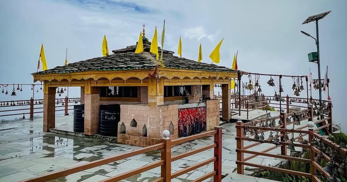 Kartik Swami Temple, Uttarakhand: How to Reach, Fare, History and Complete Travel Guide 5 A stone temple courtyard with yellow flags and railings lined with hundreds of hanging bells.