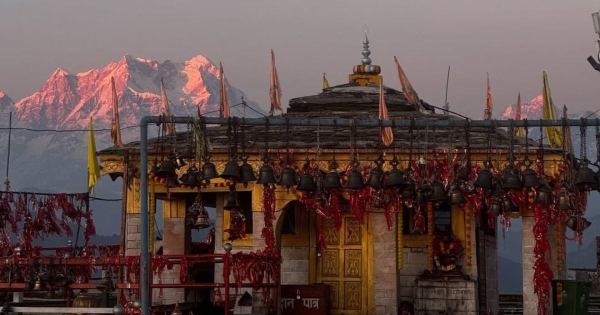 Kartik Swami Temple, Uttarakhand: How to Reach, Fare, History and Complete Travel Guide 4 Temple shrine draped in hanging brass bells, with pink-lit snowy Himalayan peaks behind it.