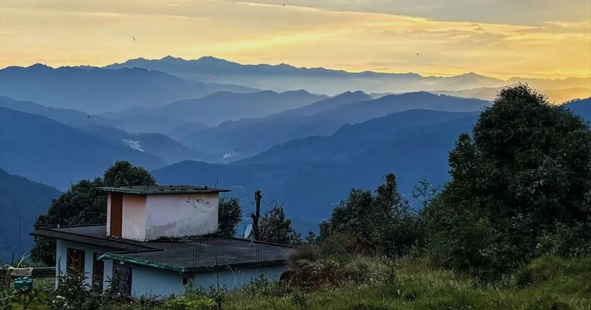 12 Best Places to Visit in Uttarakhand in October for Nature Lovers 6 A small house on a green hill overlooking layered blue mountains at sunset.
