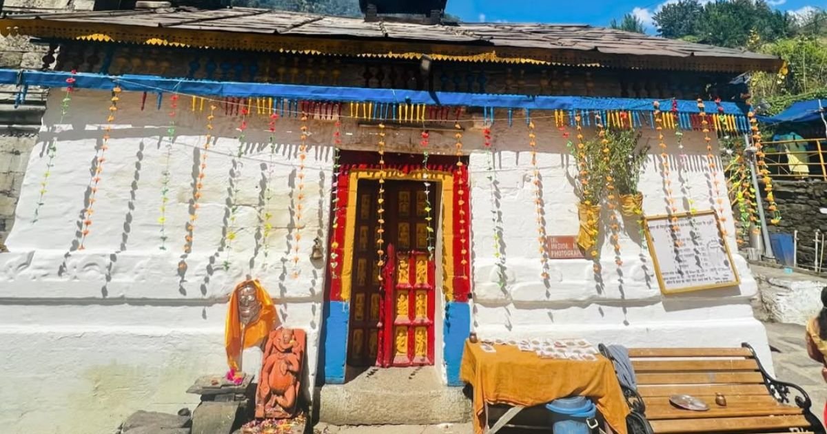 How to Reach Triyuginarayan Temple from Delhi? Your Ultimate Guide 2 Triyuginarayan Temple with a colorful red and yellow wooden doorway, decorated strings hanging down, and small idols placed outside.
