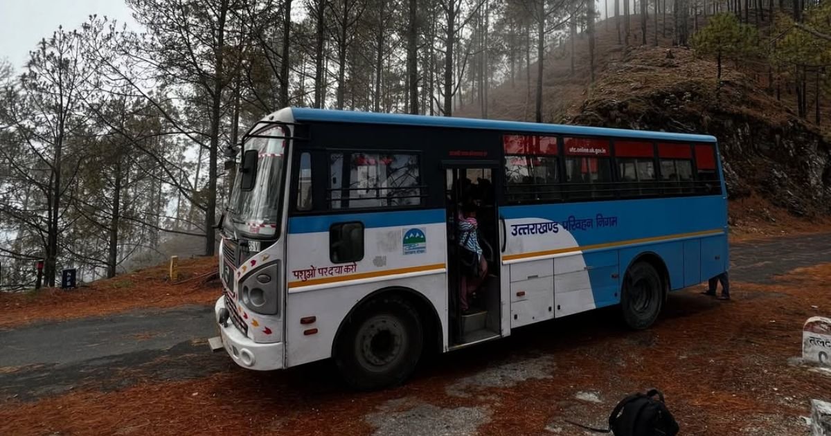 How to Reach Triyuginarayan Temple from Delhi? Your Ultimate Guide 4 A blue and white public transit bus parked on the side of a winding mountain road surrounded by tall pine trees on a misty day.