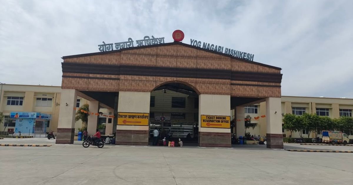 How to Reach Triyuginarayan Temple from Delhi? Your Ultimate Guide 3 The front facade of Yog Nagari Rishikesh railway station building with an arched entrance and large signs under a cloudy sky.