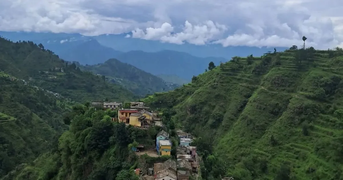 12 Best Places to Visit in Uttarakhand in October for Nature Lovers 7 A small village built on steep green hills with clouds over the mountains.