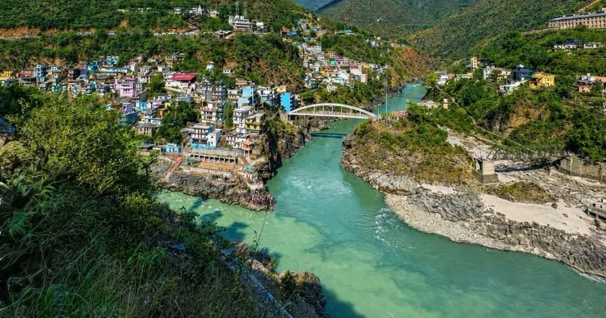 How to Reach Triyuginarayan Temple from Delhi? Your Ultimate Guide 6 High angle view of a wide turquoise river flowing through a deep valley town with buildings built on steep rocky hillsides.