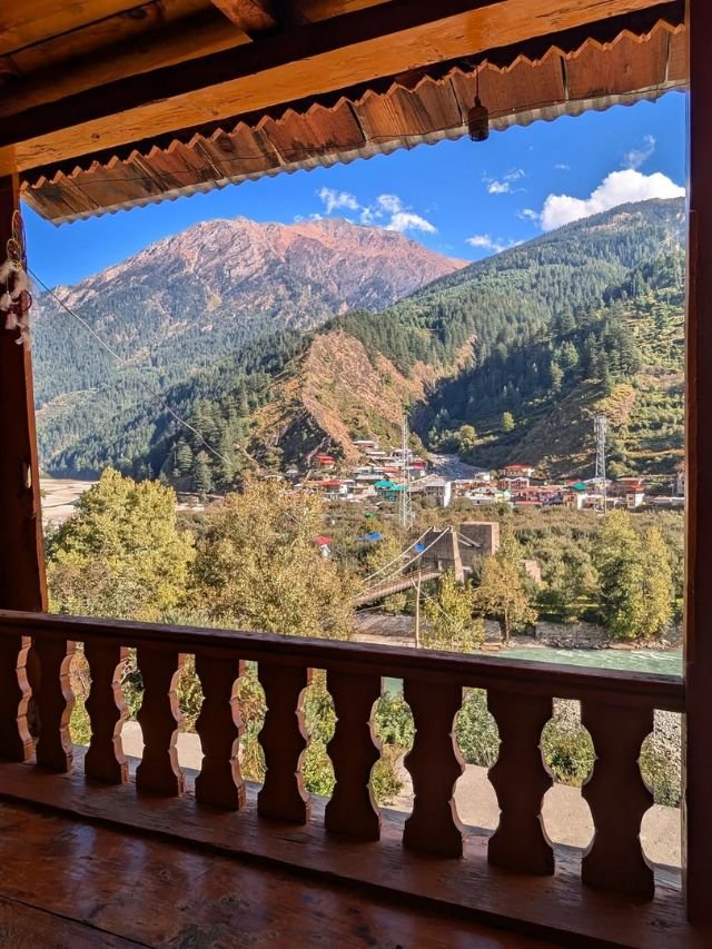 Visit Harsil Valley: How to Reach, Near Hotels, Best Time | Complete Travel Guide 16 View of a peaceful mountain village and bridge near Harshil seen via a balcony.