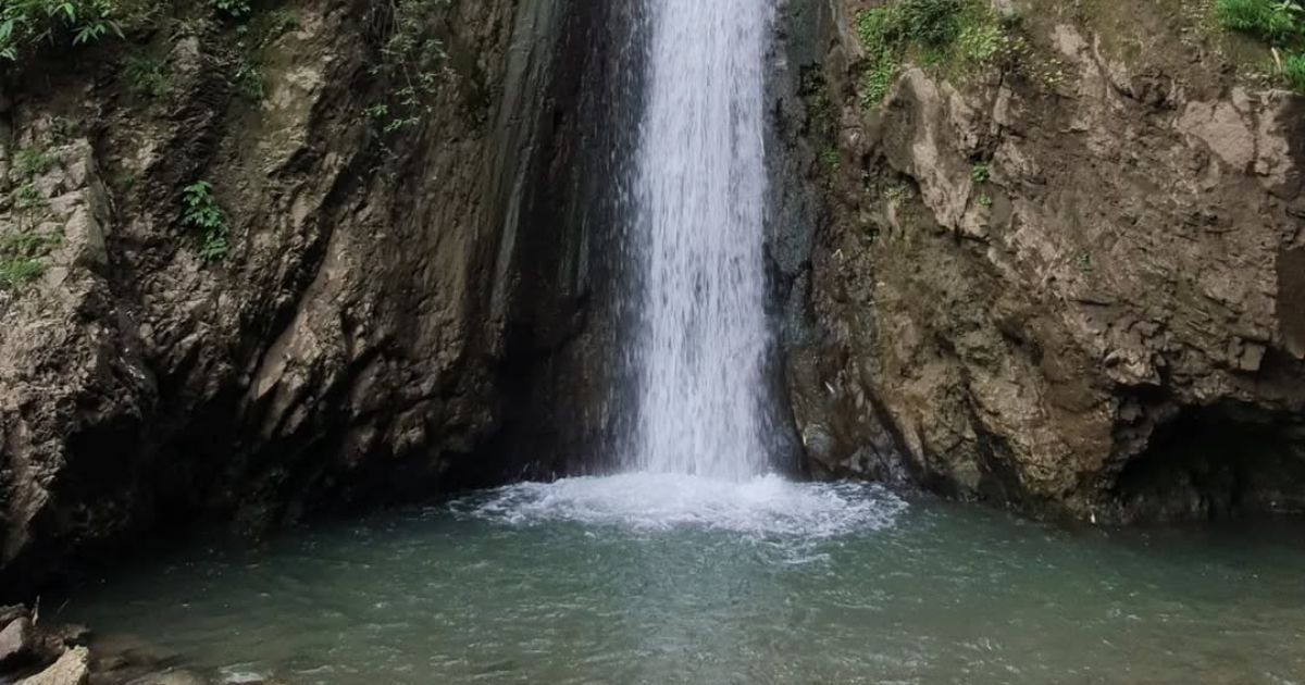 A majestic waterfall plunges down a rocky cliff into a clear pool, a refreshing sight on Easy Treks Near Dehradun.