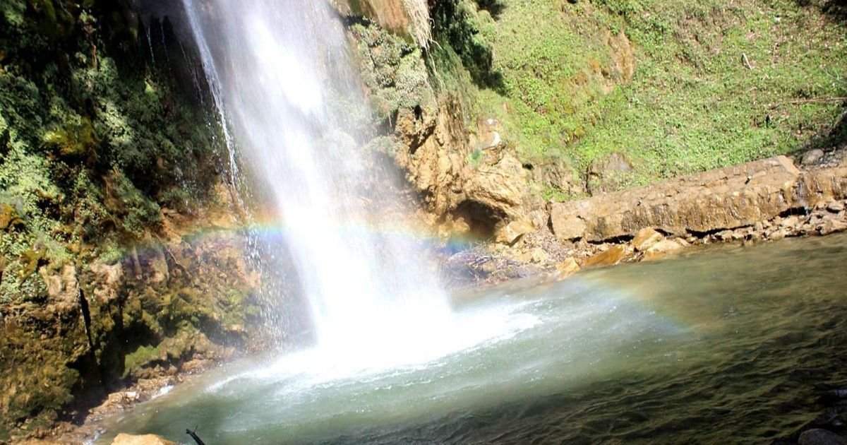 A powerful waterfall cascades into a pool, forming a small rainbow. Experience serene nature on Easy Treks Near Dehradun.