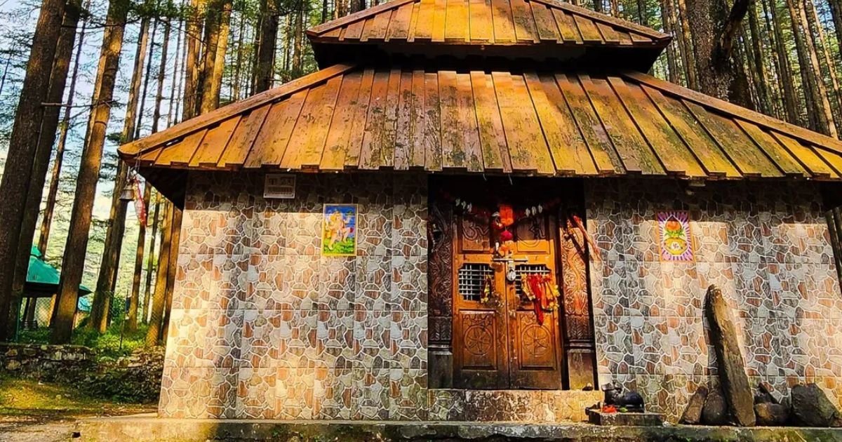 Devalsari Temple, Uttarakhand: How to Reach, Timing, History, Complete Travel Guide 6 Close up view of a stone tiled temple entrance with dark wooden doors, colorful religious posters, and a small black statue outside.