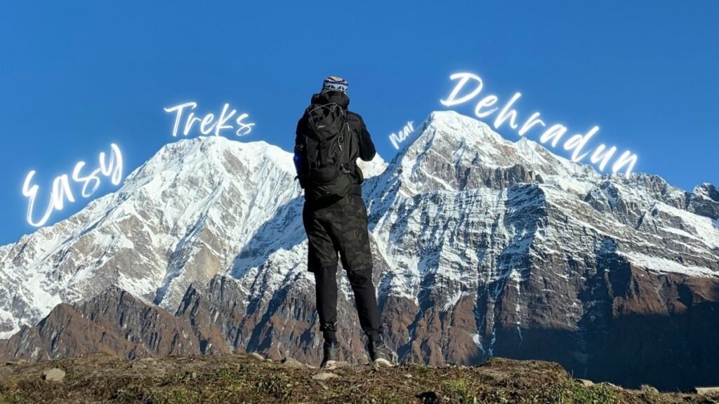 A lone hiker stands before vast snow-capped mountains under a bright blue sky, highlighting Easy Treks Near Dehradun.