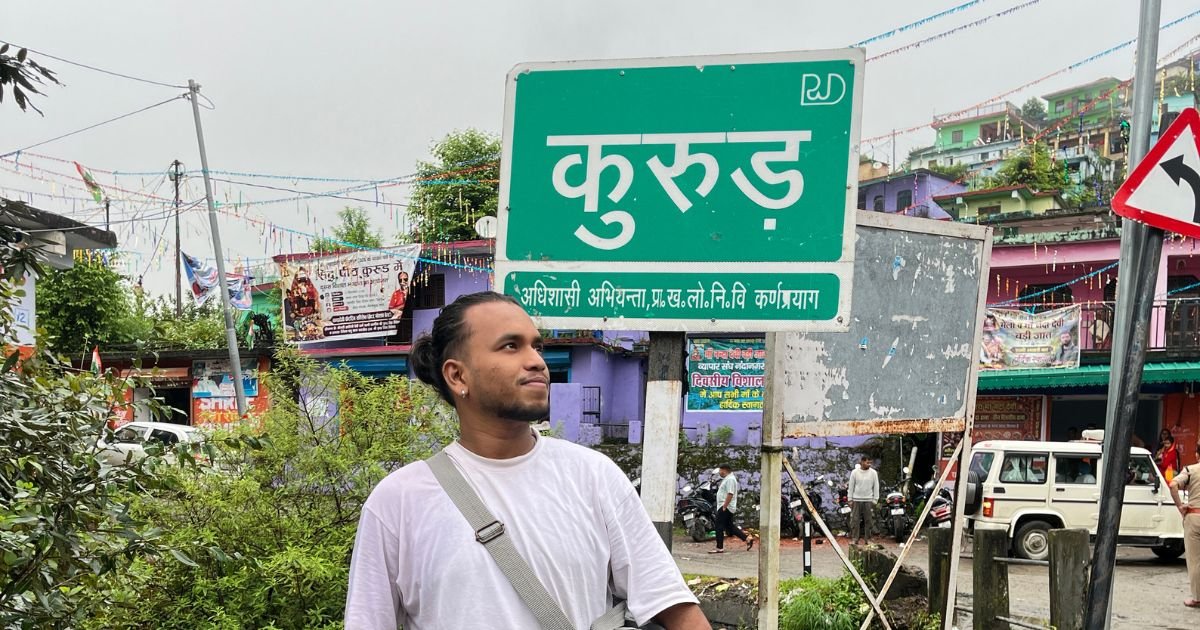 Maa Nanda Devi Badi Jaat Yatra 2026: Complete Travel Guide 5 A young man standing beside a green road sign with Kurud written in Hindi.